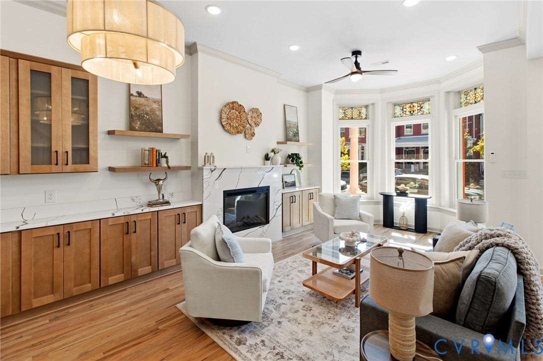 3104 E Broad Street, Richmond, VA 23223 Living area featuring wood-finish flooring, a fireplace with stone-surround, built-in wooden cabinetry, floating shelves, and a bay window with stained-glass accents
