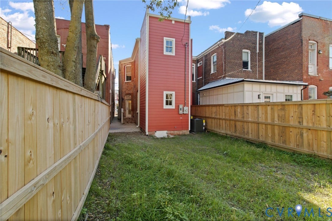 3104 E Broad Street, Richmond, VA 23223 Exterior backyard space featuring horizontal wood-slat fencing, an open lawn area, and a red lap-siding building facade