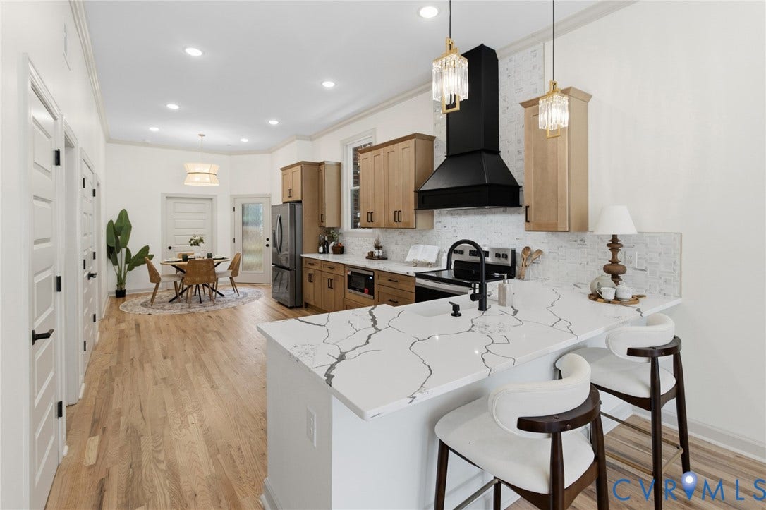3104 E Broad Street, Richmond, VA 23223 Kitchen featuring a waterfall-edge stone countertop, wood-finish cabinetry, a matte black range hood, light-toned wood-finish flooring, and pendant lighting