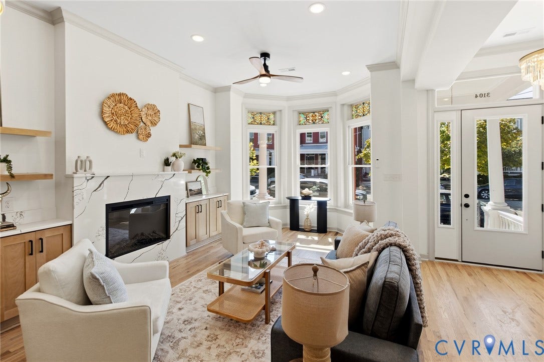 3104 E Broad Street, Richmond, VA 23223 Living area featuring hardwood flooring, a fireplace with a stone-finish surround, built-in cabinetry, custom stained-glass window transoms, and a three-paneled bay window