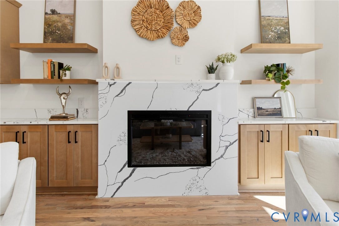 3104 E Broad Street, Richmond, VA 23223 Fireplace featuring a white surround with integrated veining, flanked by custom cabinetry with matte black hardware, stone-finish countertops, and natural wood-tone floating shelves