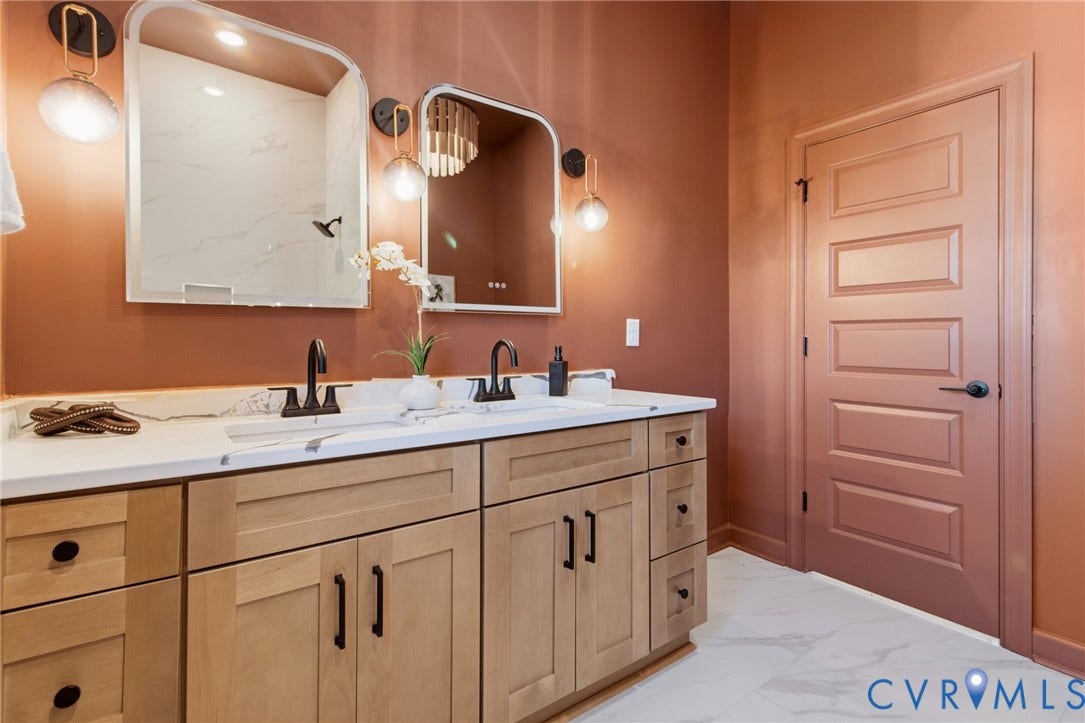 3104 E Broad Street, Richmond, VA 23223 Dual-vanity cabinetry with matte black hardware, white countertop, arched mirrors, wall-mounted globe lighting, and five-panel interior door