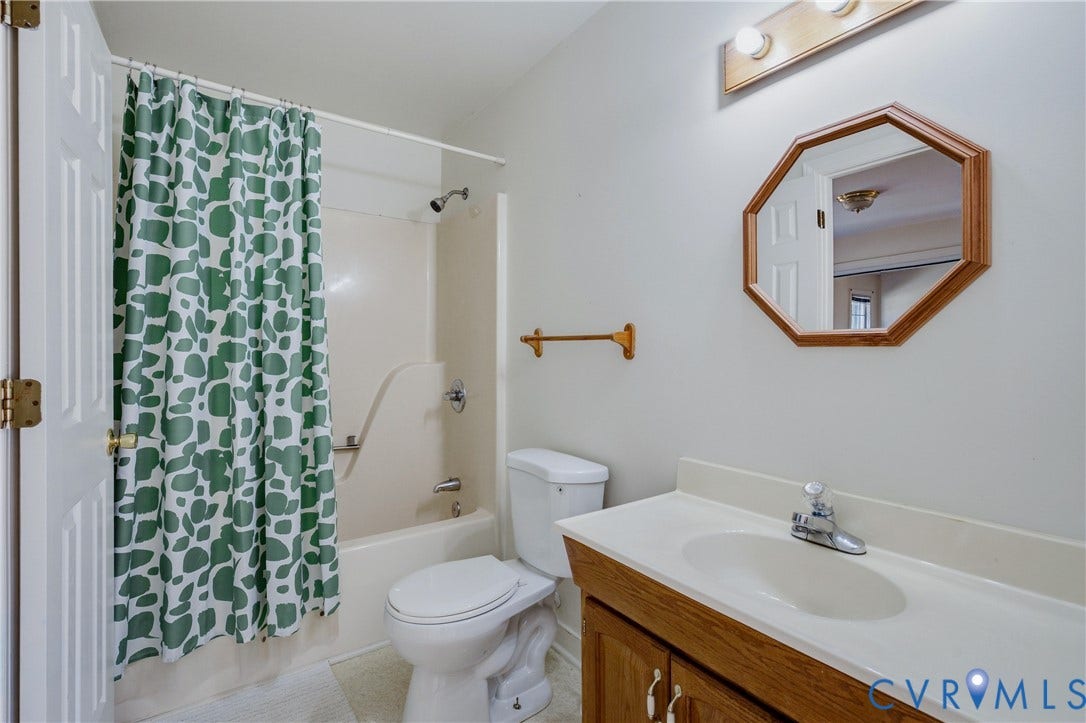 11400 County Drive, Prince George, VA 23842 Jack and jill Bathroom featuring a vanity with a molded countertop and integrated sink, wood-finish cabinetry, a tub-shower combination, and an octagonal wall-mounted mirror