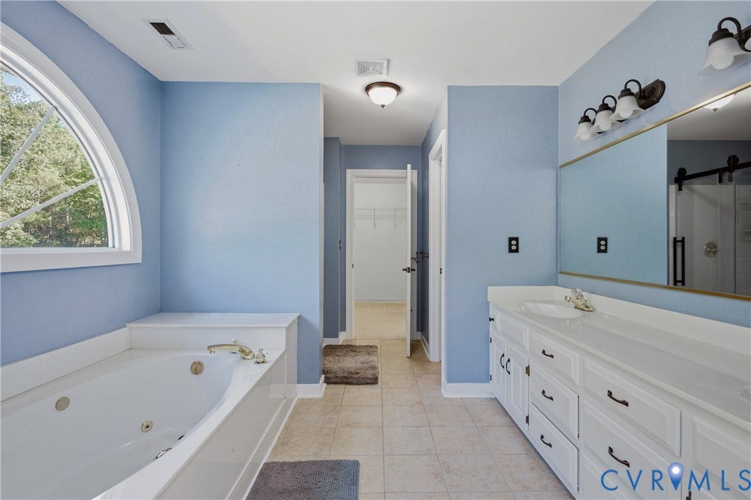 11400 County Drive, Prince George, VA 23842 Bathroom featuring an arched window, a built-in jetted soaking tub, white cabinetry, a large wall-mounted mirror, and tile flooring