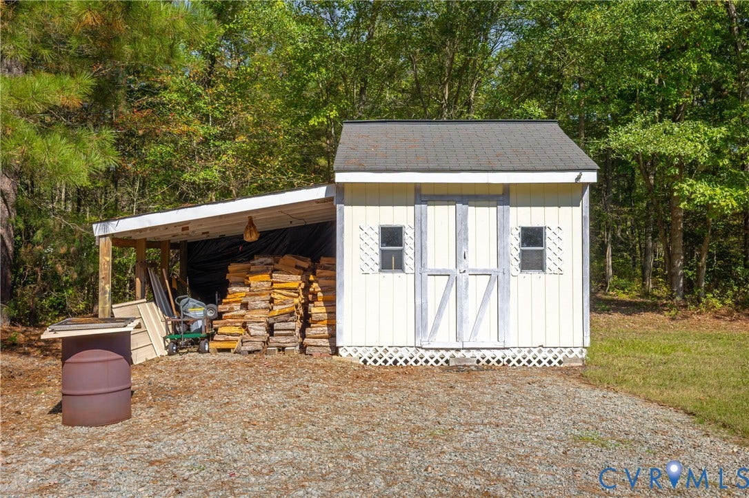 11400 County Drive, Prince George, VA 23842 Storage shed featuring vertical siding, a shingled roof, dual windows with decorative shutters, and an attached lean-to structure