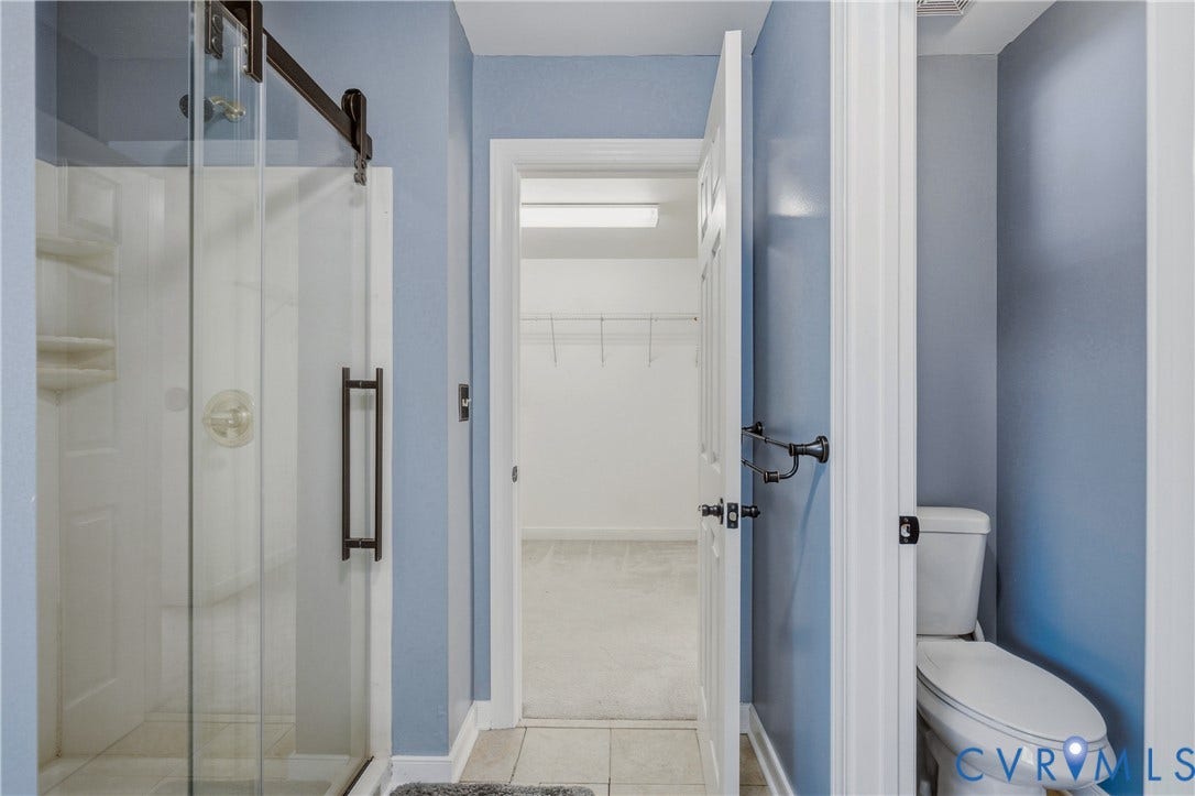 11400 County Drive, Prince George, VA 23842 Shower enclosure with a sliding glass door and dark metal hardware, tile flooring, wall-mounted towel rack, and built-in closet shelving