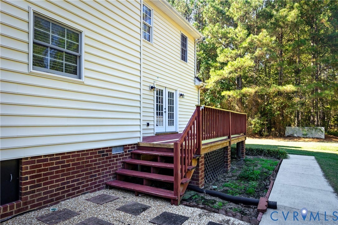 11400 County Drive, Prince George, VA 23842 Exterior side elevation featuring light-colored horizontal siding, a red brick foundation, an elevated wooden deck with matching railing, and double glass-paned doors