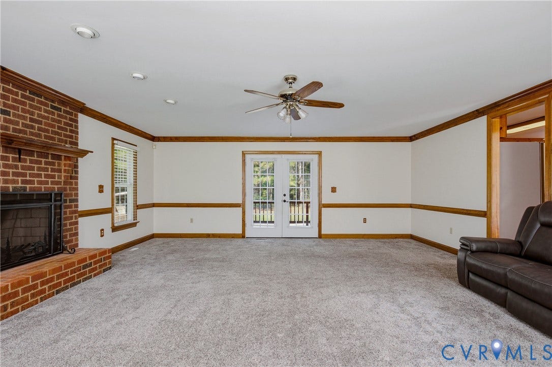 11400 County Drive, Prince George, VA 23842 Brick fireplace, wall-to-wall carpeting, ceiling fan with integrated lighting, wood-trimmed chair rails, and double glass-paneled exterior doors