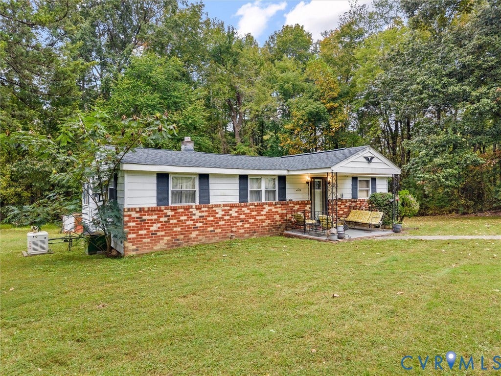 8631 Kimages Road, Charles City, VA 23030 Exterior featuring a brick and white siding facade, asphalt shingle roof, covered front porch with ornamental metal supports, and expansive tree-lined grounds