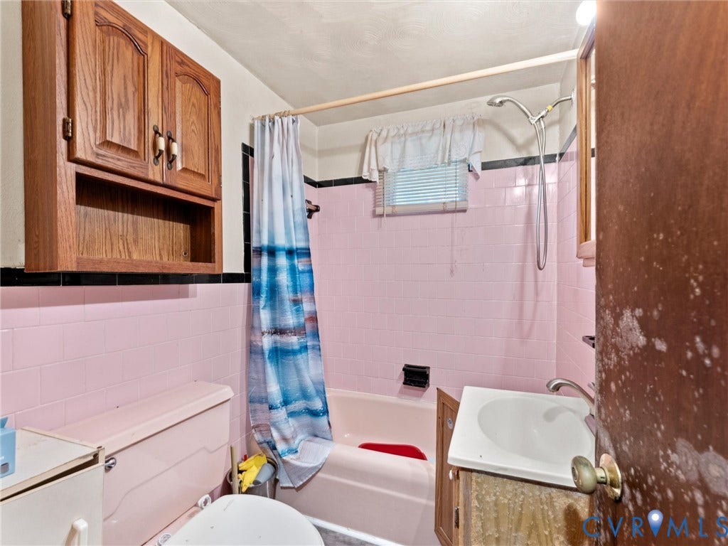 8631 Kimages Road, Charles City, VA 23030 Bathroom featuring pink wall tiling with black accent trim, wood-finish wall-mounted cabinetry, integrated bathtub, and a pedestal sink
