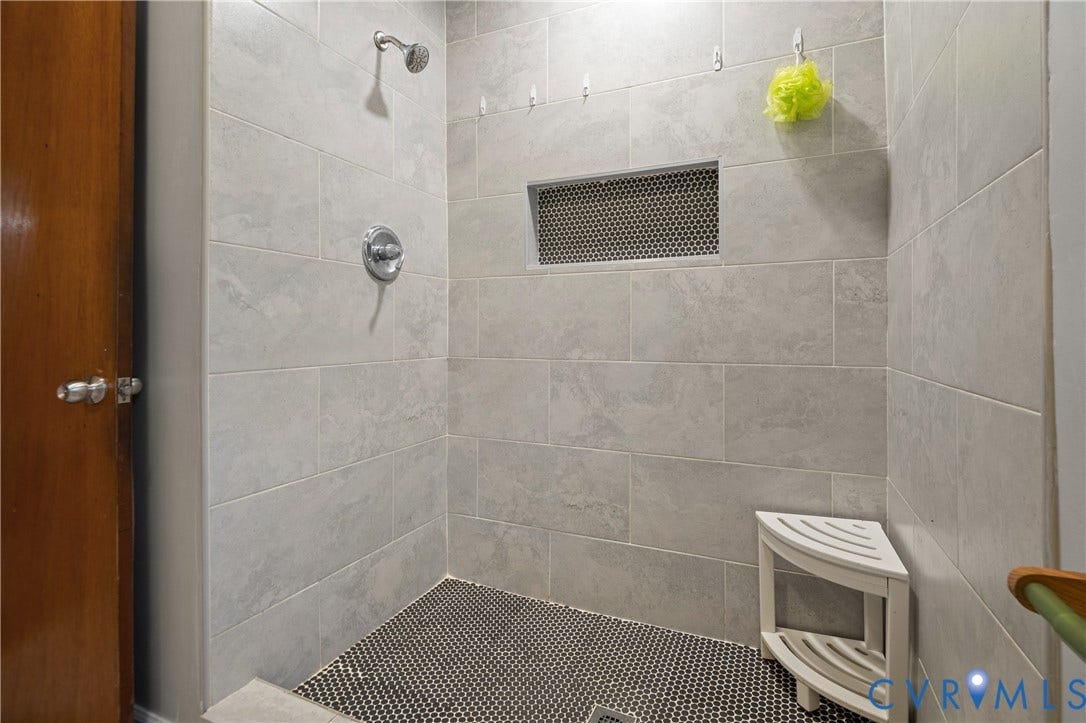9834 N Wagstaff Circle, Mechanicsville, VA 23236 Walk-in shower featuring large-format light gray wall tile, contrasting circular mosaic floor tile, built-in wall niche, and polished chrome shower fixture