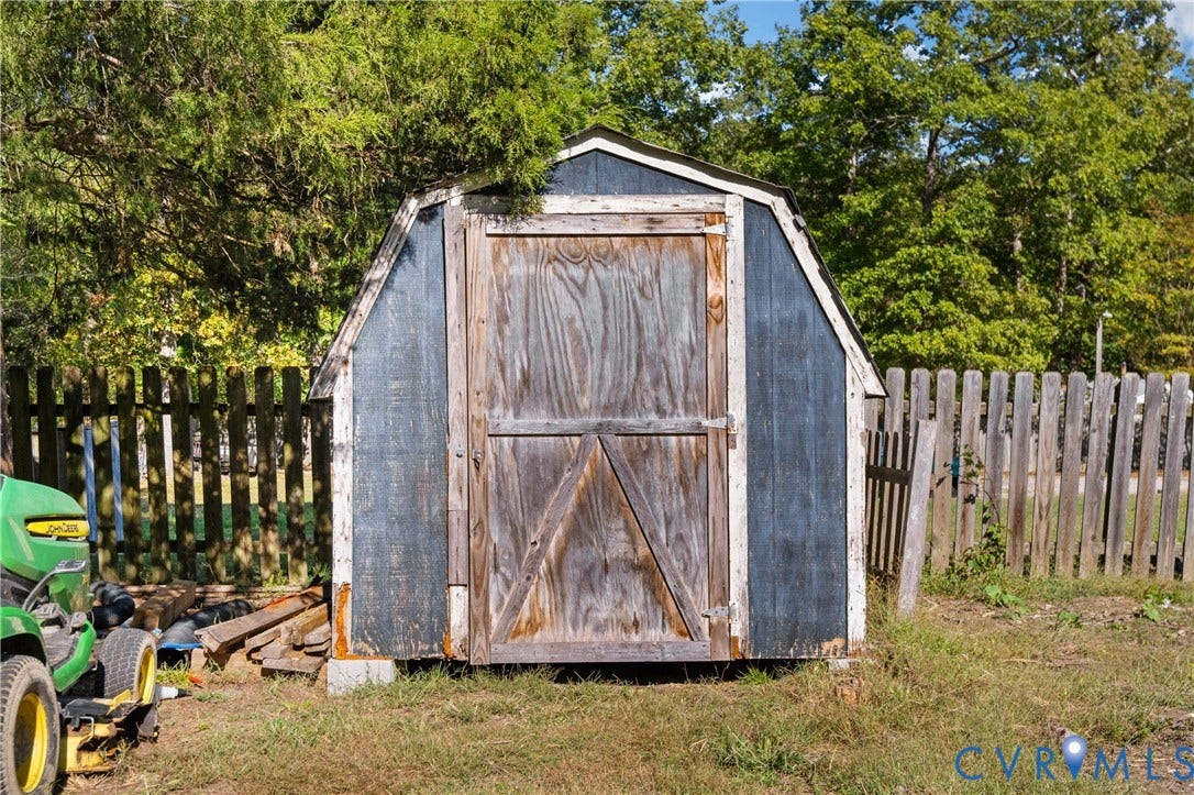 9834 N Wagstaff Circle, Mechanicsville, VA 23236 Gambrel-roof storage shed featuring wooden siding, a hinged door, and a perimeter wooden privacy fence