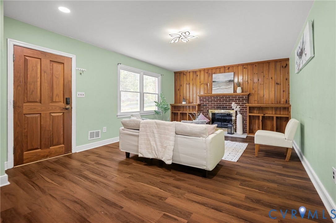 9834 N Wagstaff Circle, Mechanicsville, VA 23236 Living area featuring wood-finish flooring, wood-paneled walls, a brick fireplace, built-in shelving, and a solid wood entry door