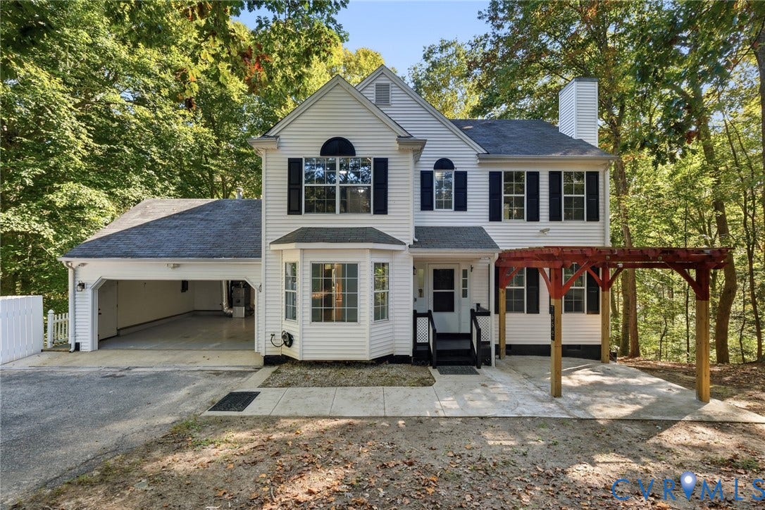 7652 Thacher Drive, Toano, VA 23168 Two-story exterior featuring white vinyl siding, a multi-pane bay window, an attached two-car garage, and a timber-frame pergola