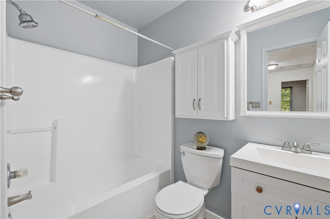 7652 Thacher Drive, Toano, VA 23168 Bathroom featuring a white vanity cabinet with an integrated rectangular sink, a framed wall mirror, a white wall-mounted storage cabinet, and a bathtub with a white surround