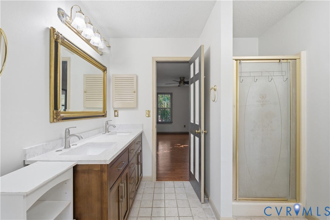7652 Thacher Drive, Toano, VA 23168 Double vanity with stone countertop, undermount sinks, wood-finish cabinetry, and glass-enclosed shower