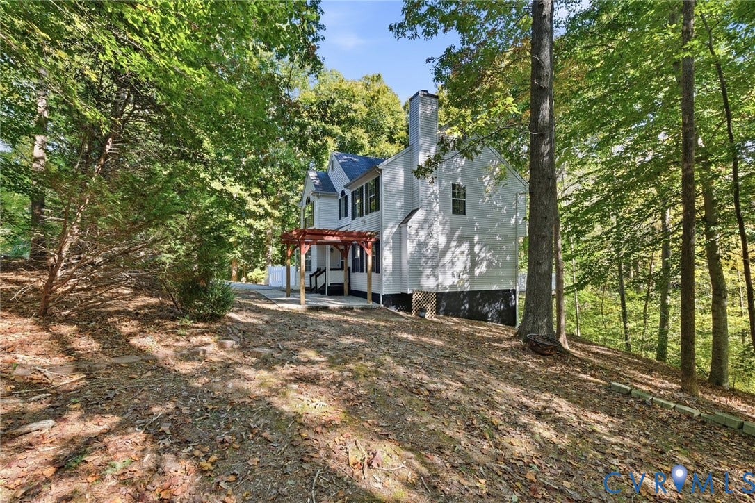 7652 Thacher Drive, Toano, VA 23168 Two-story residence featuring a painted brick exterior, a wood-frame pergola, an attached chimney stack, and mature trees