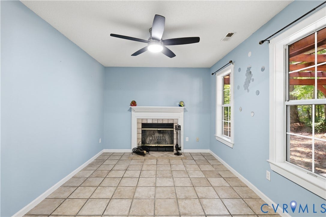 7652 Thacher Drive, Toano, VA 23168 Fireplace with a white mantel and decorative tile surround, ceramic tile flooring, multi-blade ceiling fan with integrated light, and large windows with grid muntins
