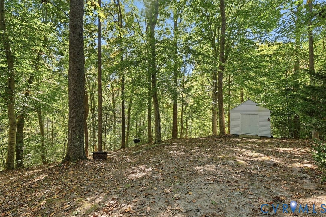 7652 Thacher Drive, Toano, VA 23168 Expansive wooded lot featuring mature trees, a natural earth surface, and a detached white-sided storage structure with double doors