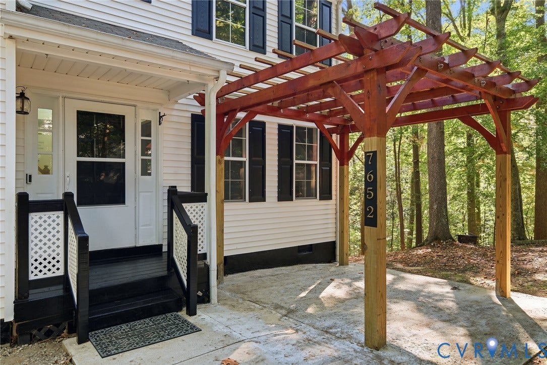 7652 Thacher Drive, Toano, VA 23168 Exterior entry featuring a wood pergola, concrete patio, white lap siding, black shutters, and stairs with decorative lattice railings