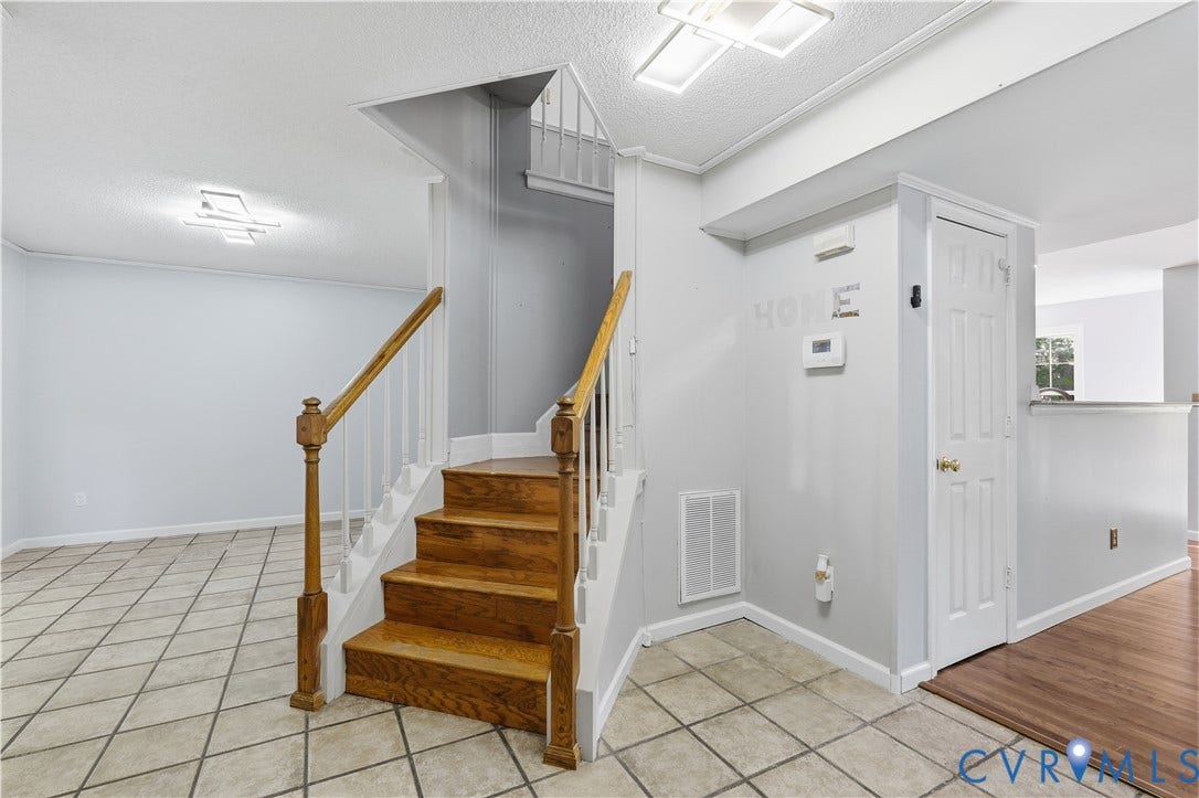 7652 Thacher Drive, Toano, VA 23168 Staircase featuring wood treads, white balusters, and a finished wood newel post, complemented by neutral tile flooring and flush-mount lighting fixtures