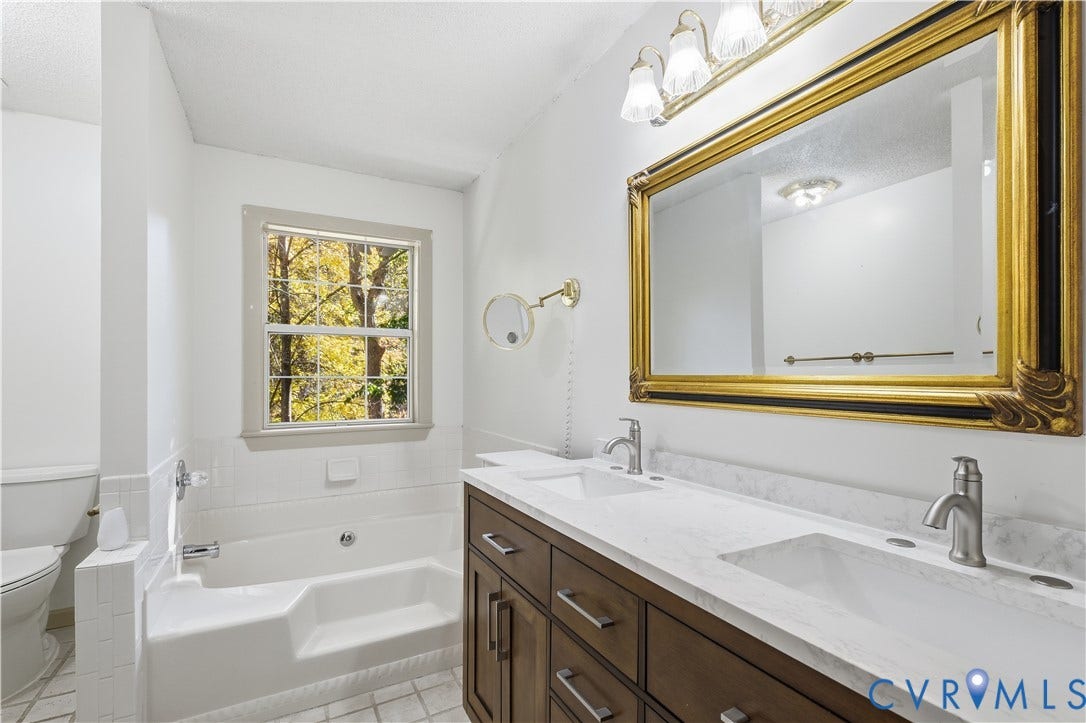7652 Thacher Drive, Toano, VA 23168 Dual vanity with stone-finish countertop, undermount sinks, wood-finish cabinetry, built-in soaking tub, and wall-mounted articulating mirror