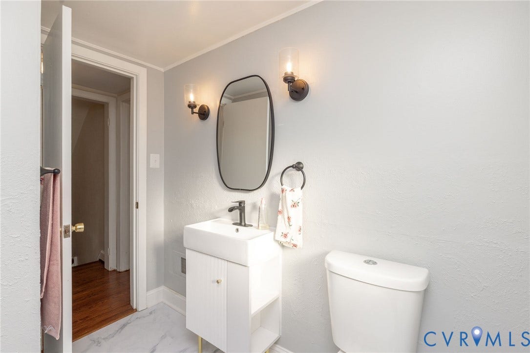 5211 W Grace Street, Richmond, VA 23226 Modern vanity with a rectangular sink, matte black faucet, oval-framed mirror, dual wall-mounted glass sconces, and stone-finish tile flooring