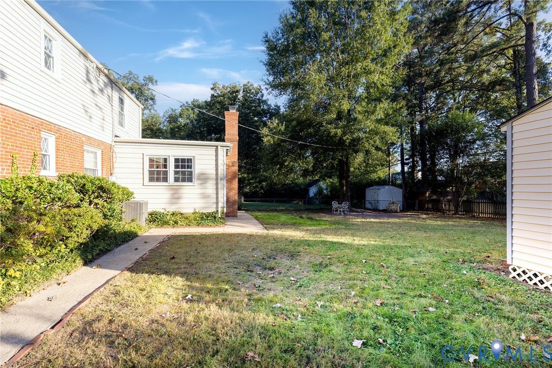 5211 W Grace Street, Richmond, VA 23226 Backyard featuring a brick and vinyl siding exterior, a brick chimney, a concrete pathway, and mature trees