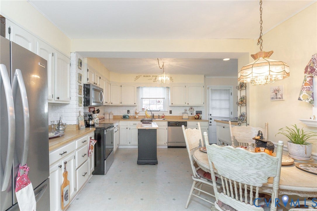 5211 W Grace Street, Richmond, VA 23226 Kitchen featuring white cabinetry, stainless steel appliances, a center island with a black finish, a brick accent column, and a decorative pendant light fixture