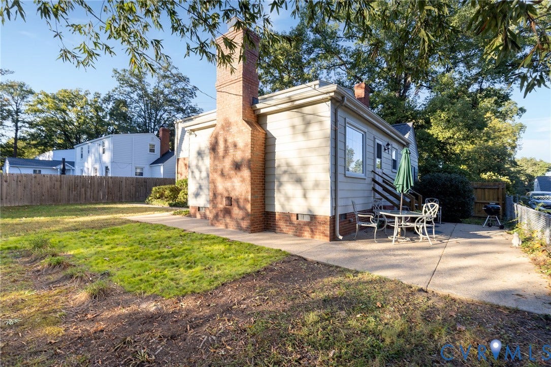 5211 W Grace Street, Richmond, VA 23226 Exterior featuring horizontal siding, a prominent brick chimney, concrete patio, and a wood privacy fence