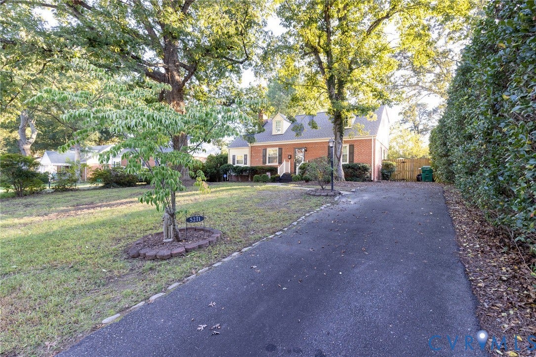 5211 W Grace Street, Richmond, VA 23226 Brick exterior featuring a multi-gabled roofline, dormer windows, shuttered window accents, and a paved driveway set within a treed lot