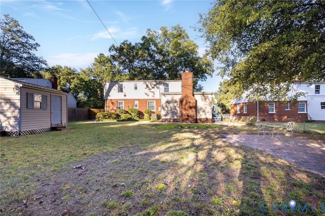5211 W Grace Street, Richmond, VA 23226 Expansive backyard featuring a brick patio, detached storage structure with vinyl siding, exterior brick chimney, and mature trees