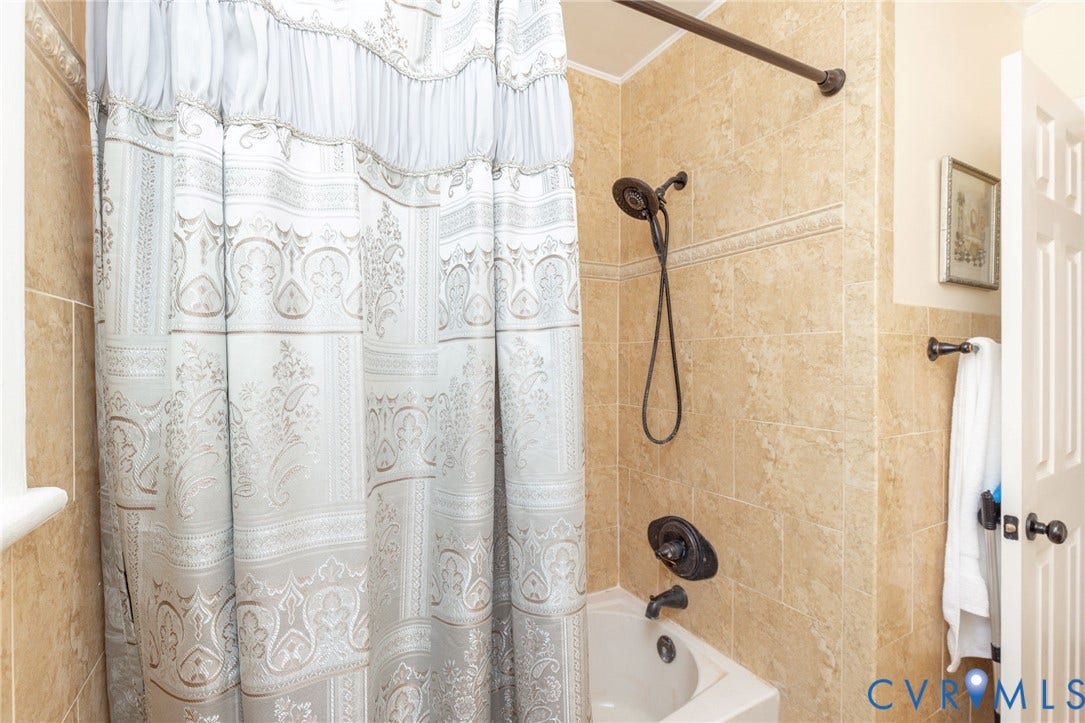 5211 W Grace Street, Richmond, VA 23226 Shower and tub combination featuring floor-to-ceiling tile surround with decorative crown molding trim, dark oil-rubbed bronze fixtures, and a multi-setting handheld showerhead
