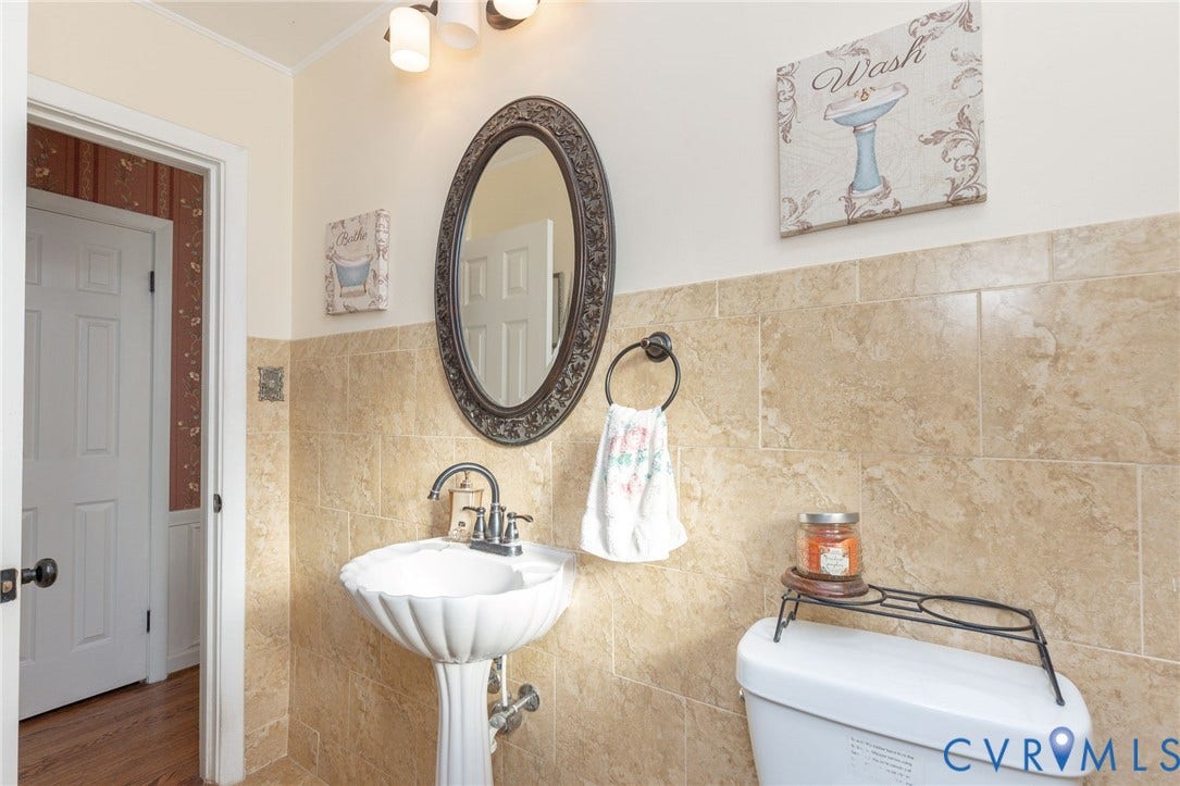 5211 W Grace Street, Richmond, VA 23226 Pedestal sink with a dual-handle faucet, oval mirror with an ornate frame, and tiled wall surfacing