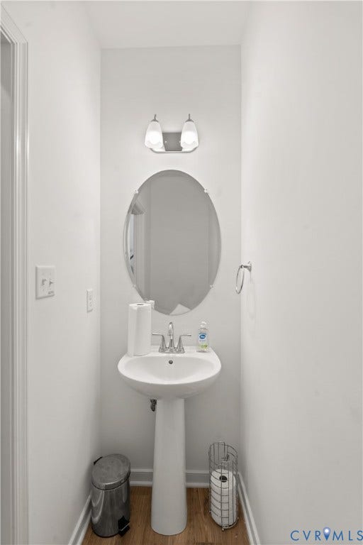 13807 Denleigh Court, Midlothian, VA 23112 Pedestal sink with a polished chrome faucet, oval frameless mirror, and dual-light wall-mounted fixture, complemented by wood-finish flooring