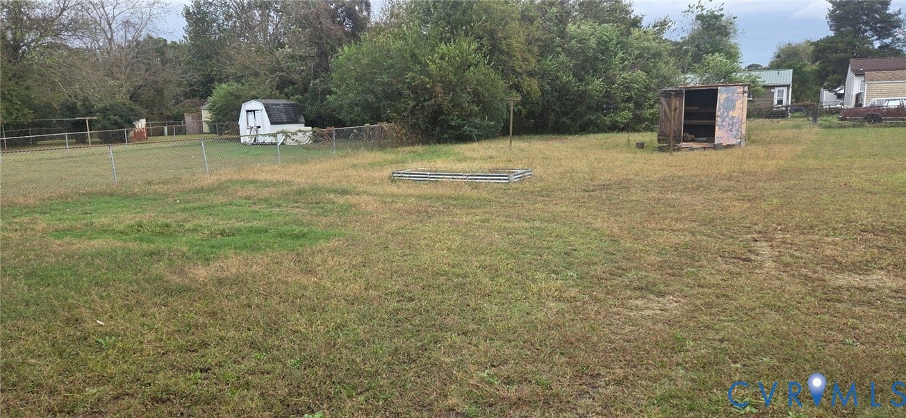 1342 Steel Street, Petersburg, VA 23803 Expansive level lot featuring mature trees, chain-link perimeter fencing, and dual detached storage structures