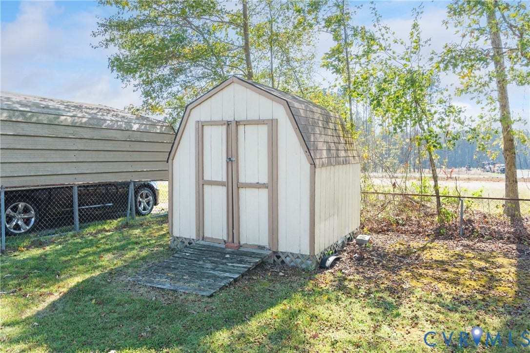 542 Petty Street, Petersburg, VA 23805 Gambrel-style storage shed with double-door entry, wood-paneled siding, and shingled roof, set on a grass-covered lot with chain-link perimeter fencing
