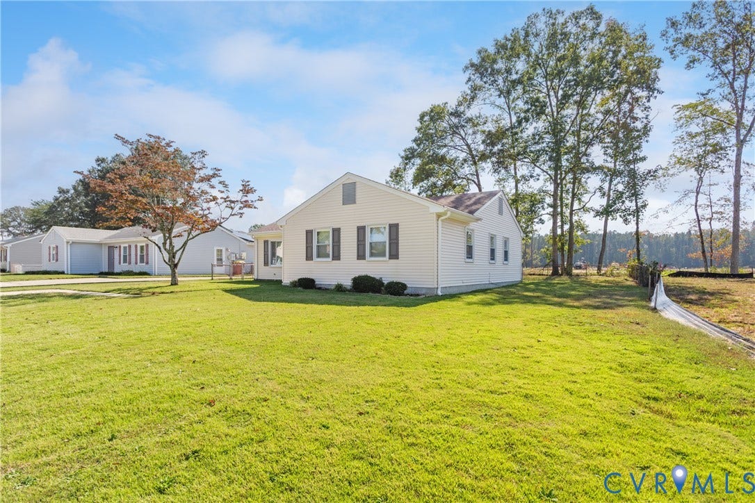 542 Petty Street, Petersburg, VA 23805 Single-story residence with light-colored horizontal siding, dark decorative window shutters, and a gable roofline situated on a sprawling parcel featuring expansive grass lawn and mature perimeter trees