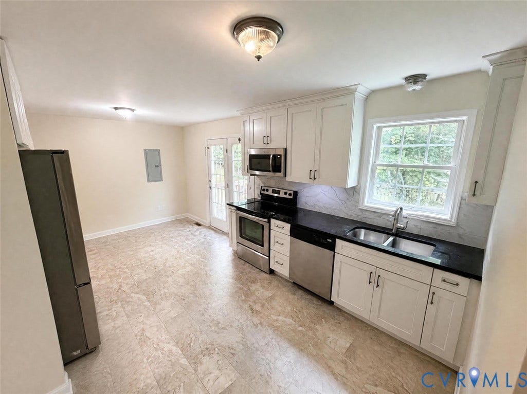 Kitchen featuring white shaker-style cabinetry, dark stone countertops, stone-patterned tile flooring, stainless steel appliances, and a double-basin stainless steel sink