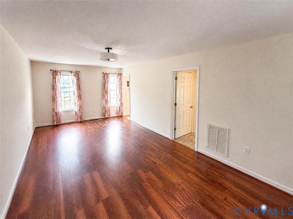 Interior space featuring wood-finish flooring, two large windows, neutral wall paint, and a ceiling-mounted light fixture