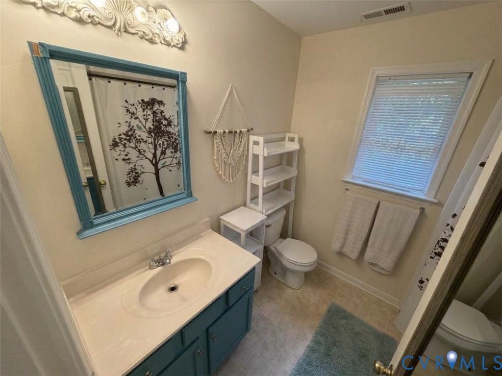Bathroom featuring a vanity with a solid-surface countertop and integrated sink, a color-coordinated framed wall mirror, a multi-light fixture, and a window with integrated blinds