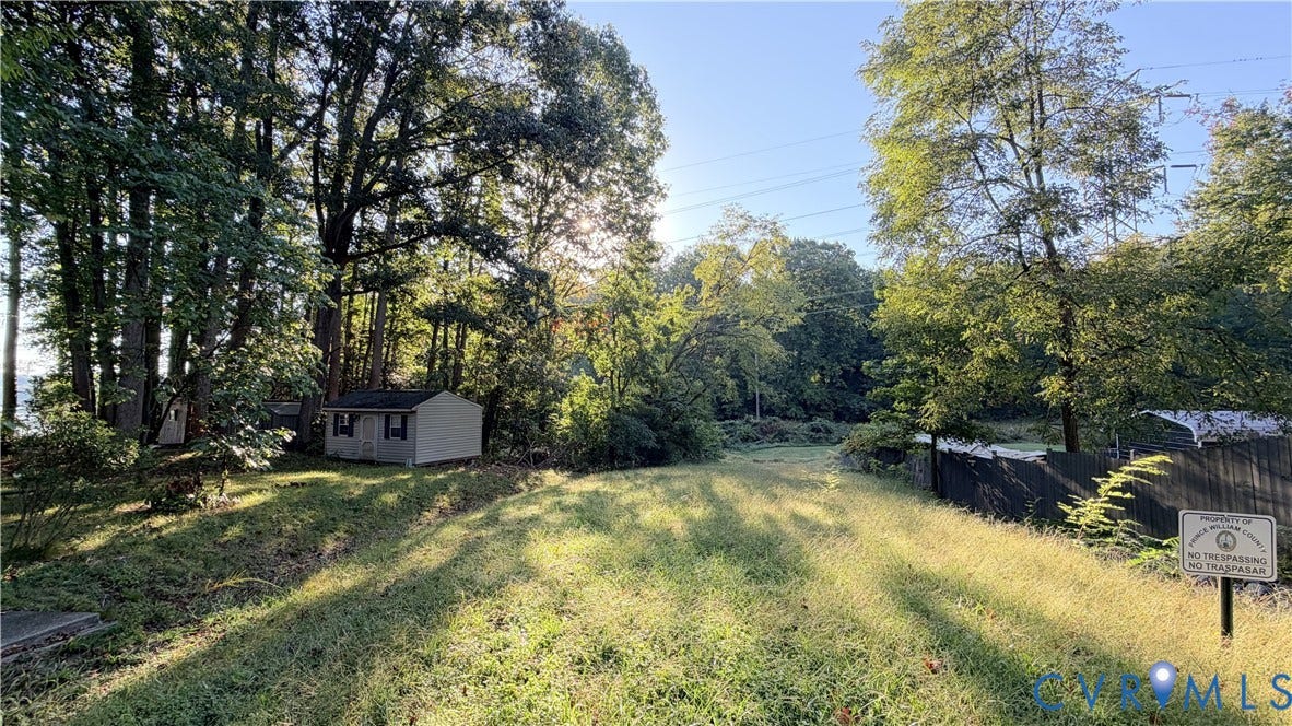 Expansive lot featuring mature trees, a detached storage structure, and perimeter wood fencing