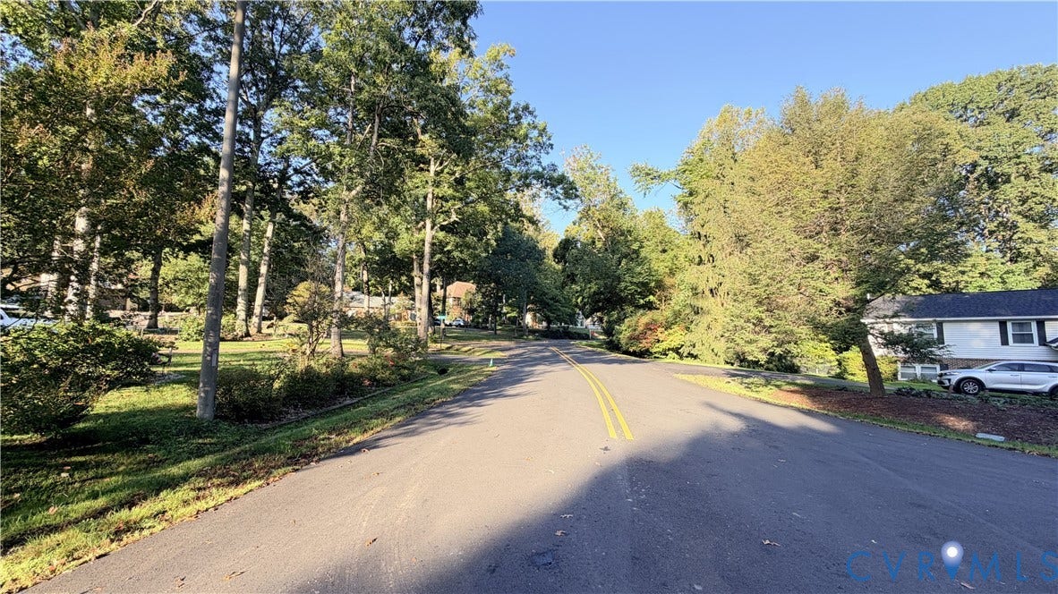Asphalt street lined with mature deciduous trees and established landscaping
