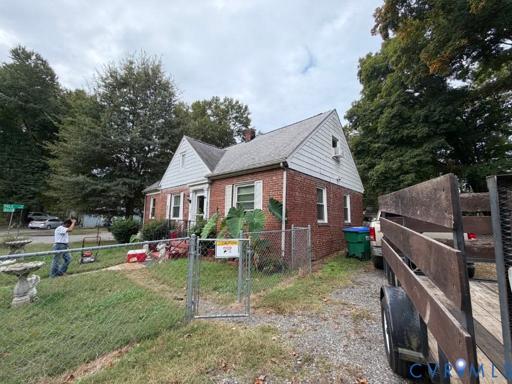Brick exterior featuring a gabled roofline, light-colored siding accents, and a chain-link fenced perimeter