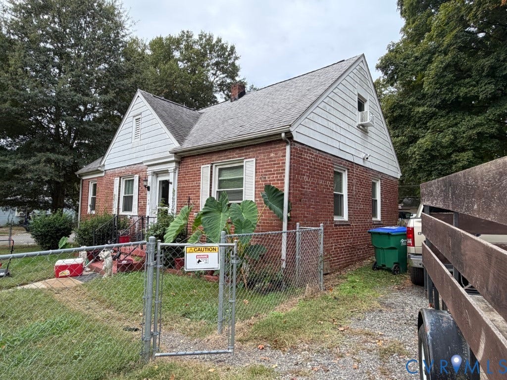 Single-story brick exterior featuring a gable roofline, white horizontal siding, window shutters, and a gated chain-link fence