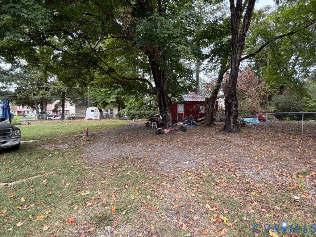 Expansive grounds featuring mature trees, partial chain-link fencing, and a detached structure
