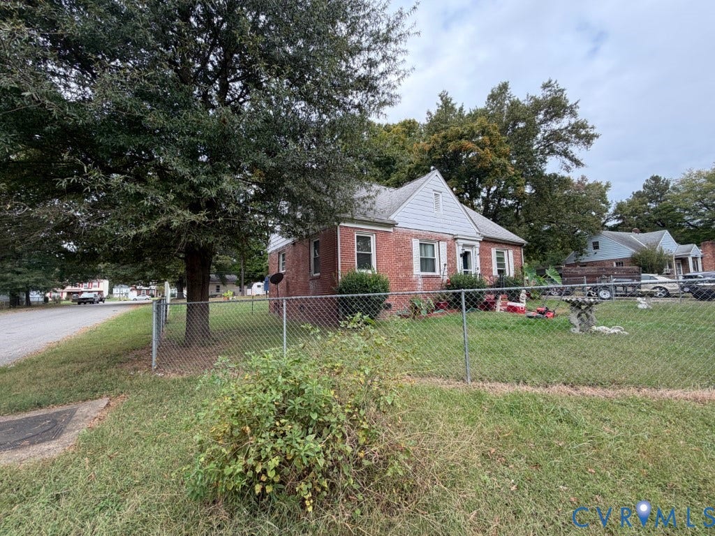 Brick exterior, gabled roofline, metal chain-link fencing, and mature trees
