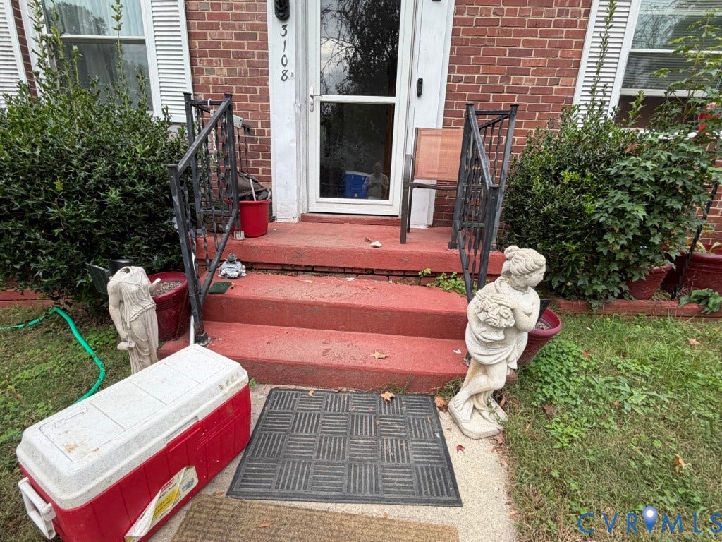 Brick exterior facade featuring a front entrance with concrete steps and black metal railings