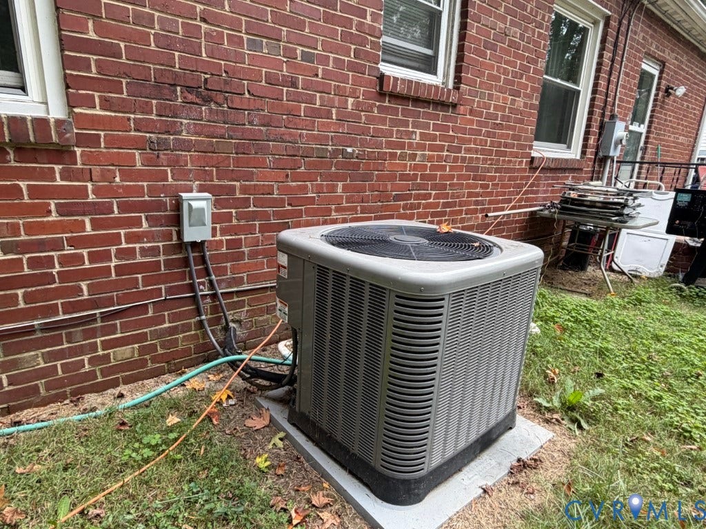 Exterior central air conditioning unit positioned on a concrete slab against a red brick facade with double-hung windows