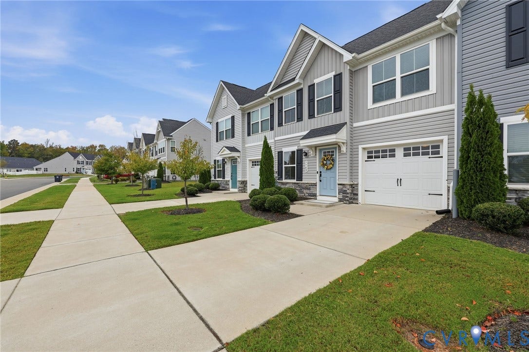 Multi-story exterior featuring gray vinyl siding, stone veneer accents, an attached garage, and a concrete driveway